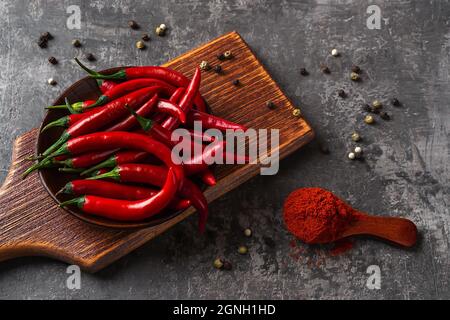 Gemahlener Chilischote in einem Holzlöffel in der Nähe von frischen roten Chilischoten auf einem Schneidebrett. Chilischote als würzige Zutat für scharfe Gerichte. Stockfoto