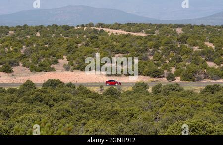 Ein rotes Auto fährt entlang einer Landstraße in New Mexico. Stockfoto