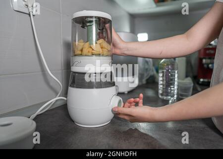 Nahaufnahme des elektrischen Mixers in der Hand einer unbekannten Frau, die ihn auf der Küchentheke hält, die Kartoffelbrei zubereitet Stockfoto