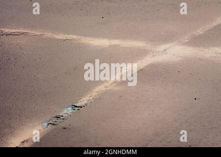 Eine Nut im Asphalt, die ein Fadenkreuz bildet. Nach Regen bleibt Wasser auf dem Asphalt. Stockfoto