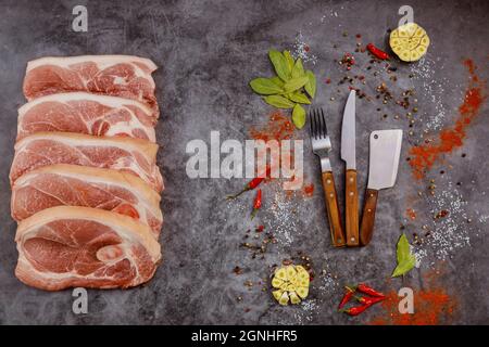 Scheiben rohes Schweinekotelett mit Gewürzen und Messer auf grauem Hintergrund. Draufsicht. Stockfoto