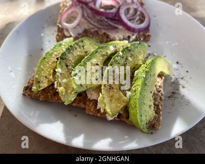 Leuchtend grüne Avocado-Scheiben auf Crackerbrot mit roter Zwiebel im Hintergrund. Stockfoto