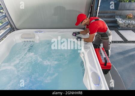 Kaukasischer Whirlpool professioneller Techniker in seinen 40er Jahren, der Systemcontroller unter modernen Wohngazebos überprüft. Home Erholung Thema. Stockfoto