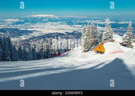 Schneebedeckte Winterlandschaft und schneebedeckter Pinienwald. Kleine schneebedeckte Berghütte am Hang, Poiana Brasov, Karpaten, Siebenbürgen, Rumänien, Europa Stockfoto