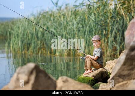 Kleiner Junge sitzt auf Stein und fischt Stockfoto