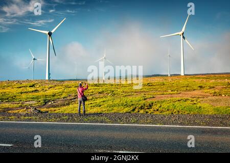 Tourist macht ein Bild von Windturbinen im Morgennebel. Fantastische Sommeransicht der Färöer Inseln, Königreich Dänemark, Europa. Ökologie Konzept Backg Stockfoto