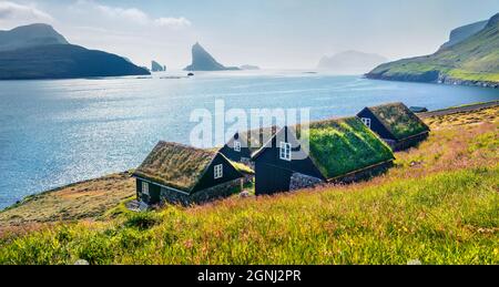 Atemberaubende Sommerszene von Bour Village mit typischen Turf-Top-Häusern und Tindholmur Klippen im Hintergrund. Panoramablick auf die Insel Vagar, Färöer, Stockfoto