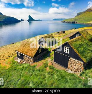 Blick von der fliegenden Drohne. Fesselnde Sommerszene von Bour Village mit typischen Turf-Top-Häusern und Tindholmur Klippen im Hintergrund. Morgenansicht aus der Luft Stockfoto