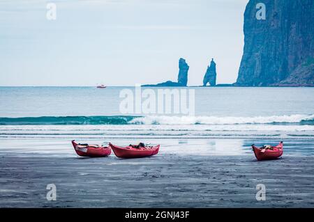 Drei rote Kanus an der Atlantikküste. Schöne Morgenlandschaft der Insel Streymoy mit Eiskollur Klippen im Hintergrund, Färöer Inseln, Königreich De Stockfoto