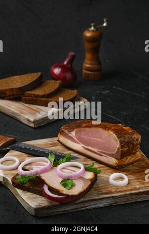 Ländliches Sandwich mit geräuchertem Speck und braunem Brot auf Holzschneidebrett Stockfoto