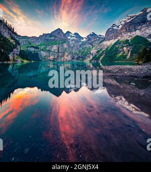 Dramatischer Sommeruntergang auf dem einzigartigen See - Oeschinen (Oeschinensee), UNESCO-Weltkulturerbe. Rote Wolken spiegeln sich in der ruhigen Wasseroberfläche. Bern Stockfoto