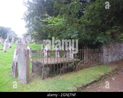 Ein Blick auf die Grabstätten der Monigaff (Minnigaff) Kirche oder Kirk , in der Nähe von Newton Stewart, Dumfries und Galloway, zeigt eines der tafel förmigen Gräber mit original umlaufenden Metallschienen. Die 'neuere' Kirche ist eine Kirche unter dem B-Denkmalschutz, die 1836 nach einem neugotischen Entwurf von William Burn erbaut wurde. Innerhalb des gleichen Geländes befinden sich die Ruinen der alten Kirche mit dazugehörigen Begräbnissen, die mit alten Grabsteinen markiert sind. Es wurde an der Stelle eines älteren motte- und bailey-Schlosses errichtet Stockfoto