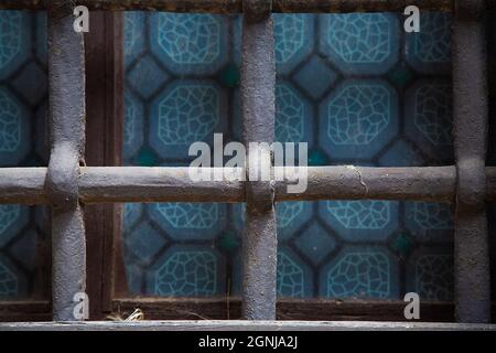 Gusseisernes Gitter am Fenster mit blauem Buntglas. Hintergrund und Hintergrundbild Bild. Quadratische geometrische Komposition. Speicherplatz kopieren. Sicherheit Stockfoto