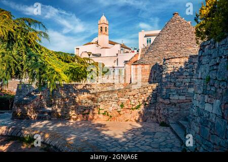 Morgenansicht von strret mit trullo (trulli) - traditionelle Apulische Trockensteinhütte mit einem konischen Dach. Frühling Stadtbild von Alberobello Stadt mit Edicol Stockfoto