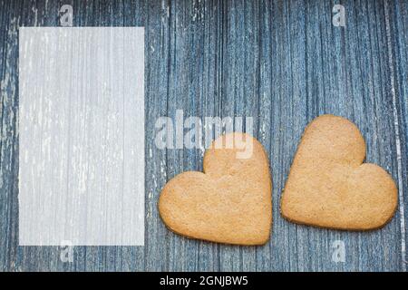 Grauer Holzhintergrund mit halbtransparentem Kopierraum und Ingwerbrot-Keksen auf der rechten Seite. Rahmen der St.-Valentinen. Einladung zur Liebe und Hochzeit Stockfoto