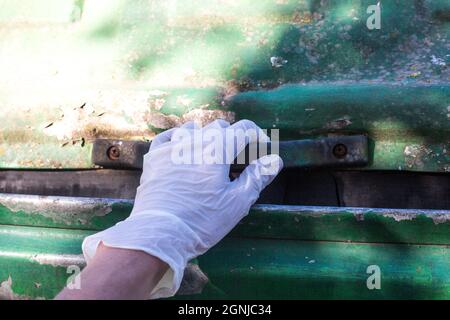 Frauenhand in weißem medizinischen Handschuh, der einen Abfalleimer öffnet. Covid- und anderer Krankheitsschutz. Hygiene bei der Abfallrecycling. Neue Regeln für die Selbstsicherheit Stockfoto