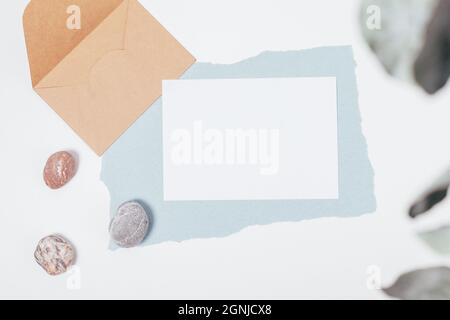 Flache, leere Einladungskarte mit Umschlag und Steinen auf weißem Hintergrund Stockfoto