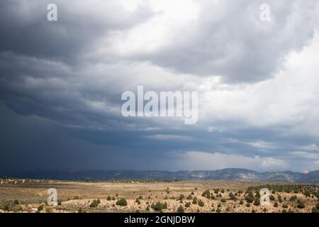 Dramatischer Himmel mit dunklen Sturmwolken und fernem starken Regen, der an einem sonnigen Tag über Ebenen und Bergen in der Ferne niederfällt Stockfoto