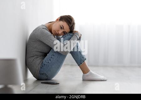 Gelangweilt verärgert depressive Dame auf dem Boden mit Smartphone sitzen, gleichgültig zu Seite Probleme haben Stockfoto