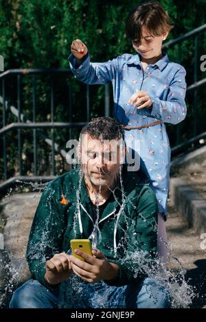 Mädchen sprengte einen mit Wasser gefüllten Ballon über den Kopf ihres Vaters Stockfoto