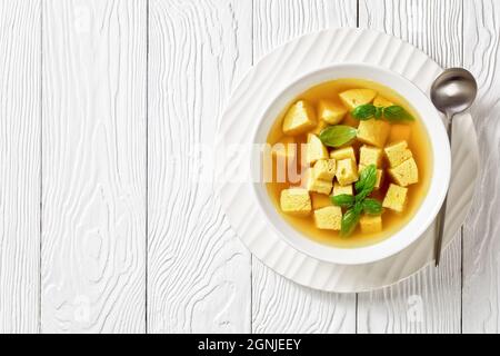 Zuppa imperiale, italienische Suppe aus Hühnerbrühe mit Parmesan-Eierknödeln, bestreut mit geriebenem Käse und Basilikum in einer Schüssel auf einem Holztisch, flach la Stockfoto