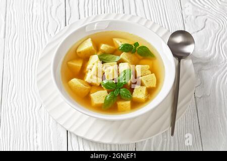 Zuppa imperiale, italienische Suppe aus Hühnerbrühe mit Parmesan-Eierknödeln, bestreut mit geriebenem Käse und Basilikum in einer weißen Schüssel auf einem Holztisch Stockfoto
