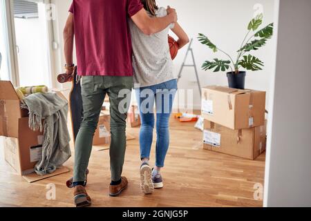 Detail, abgeschnitten Bild von jungen Mann umarmt seine weibliche Partnerin in neue Wohnung, hält Skateboard, während sie Pflege Basketball Stockfoto