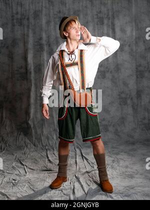 Junger Mann in einem landesbayerischen Anzug mit Shorts an Hosenträgern und Hut. Charismatisches bayerisches Porträt, schreiend und anrufend Stockfoto