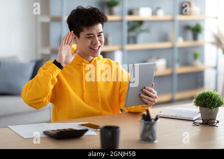 Lächelnder asiatischer Mann hält digitale Tablet winkende Hand Stockfoto