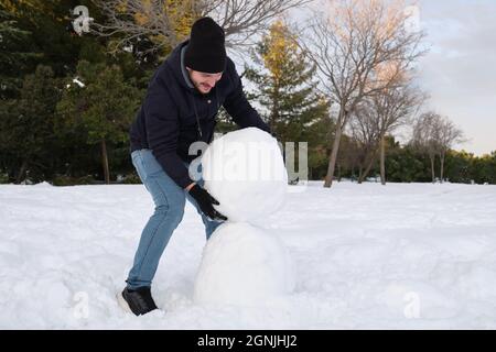 Junger Kaukasischer, der einen großen Schneeball trägt, um Schneemann zu machen. Stockfoto