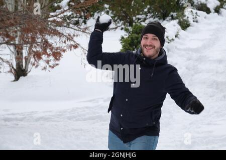 Junger Kaukasischer wirft einen Schneeball in einen Park. Stockfoto