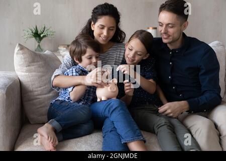 Glückliches Paar Eltern lehren kleine Kinder Sohn Tochter Geld sparen. Stockfoto