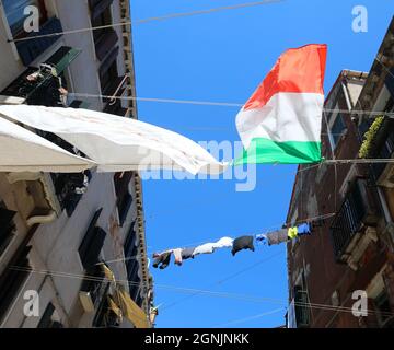 Viele Kleider hängen eine große italienische Flagge in der Gasse zwischen den Häusern Stockfoto