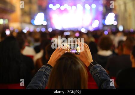 Mädchen, die ein Video mit ihrem Smartphone während eines Konzerts im Freien mit viel Publikum und die Bühne alle beleuchtet Stockfoto