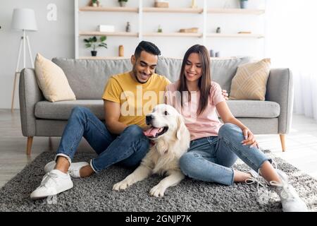 In voller Länge Porträt von fröhlichen multirassischen Paar mit ihrem Hund sitzt auf dem Boden zu Hause Stockfoto