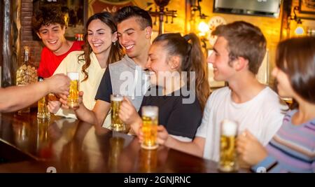 Gruppe von Millennials glücklich Freunde trinken und toasten Bier in irish Bar Restaurant. Junge Teenager Spaß zusammen in einem Vintage-Pub stehen Stockfoto