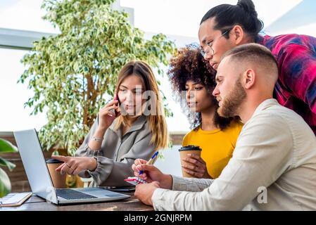Eine Gruppe junger Erwachsener diskutiert online mit dem Team in einem Coworking Space Indoor über ein ernsthaftes Startup-Projekt. Diverse Studenten arbeiten zusammen Stockfoto