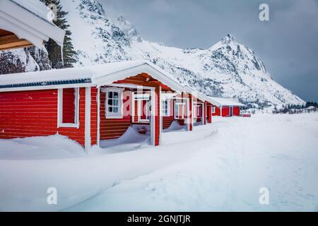 Landschaftsfotografie. Traditionelle norwegische rote Holzhäuser unter dem frischen Schnee. Düstere Winterszene der Lofoten-Inseln am Ufer des Kongsjordp Stockfoto