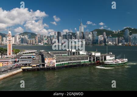 Eine Star Ferry kommt am Tsim Sha Tsui Pier in Kowloon an, mit Wan Chai und Causeway Bay, Hong Kong Island, sichtbar über den Victoria Hafen Stockfoto