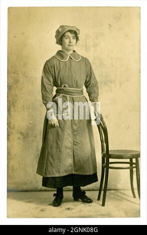 Originalpostkarte aus der Zeit des 1. Weltkriegs von einer hübschen Arbeiterin der Fabrik, mit Tunika und Mob-Mütze, möglicherweise Munitionsarbeiterin, um 1916, unbekannter Standort, Großbritannien Stockfoto