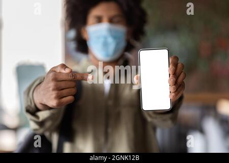 Afroamerikanischer Kerl In Medizinischer Maske, Der Smartphone Mit Leerem Weißen Bildschirm Demonstriert Stockfoto