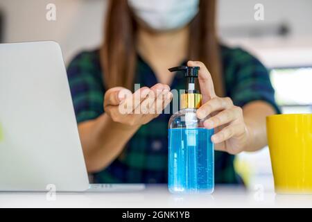 Nahaufnahme Asiatische Frau Hand mit Handdesinfektionsmittel, wenn sie zu Hause mit Technologie-Laptop und Mobiltelefon in der Küche arbeitet, zu Hause in Covid-1 Stockfoto