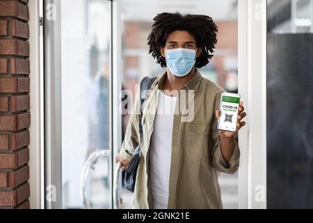 Junger Afrikaner Demonstriert Internationales Covid-19 Zertifikat Auf Smartphone Am Eingang Des Gebäudes Stockfoto