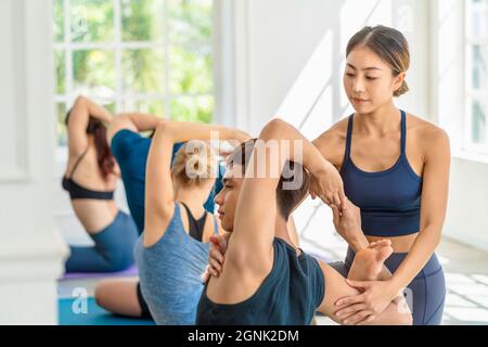 Gruppe von Vielfalt Yoga Sport Menschen üben mit ihrem Coaching in Yoga-Klasse, asiatische Yoga-Ausbilderin Frau unterstützen jungen asiatischen Sportmann für Yoga tr Stockfoto