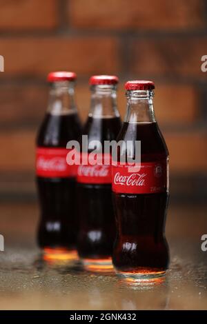 RIVNE, UKRAINE JUNI 26 2020: Drei klassische Glasflaschen von Coca-Cola auf Backsteinwand. Dosen von Coca-Cola. Stockfoto