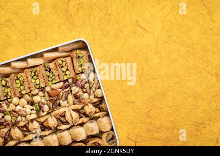 Auswahl an traditionellem türkischen Baklavagebäck in einer Blechdose gegen handgemachtes Papier mit Kopierfläche, ein Dessert ist auch als persisch oder leb bekannt Stockfoto