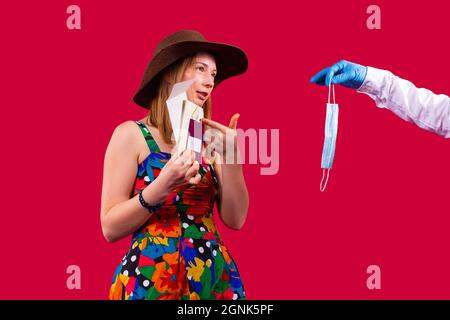 Hübsche Frau in einem farbigen Kleid mit Cowboy-Hut zeigt auf den Impfpass und braucht keine medizinische Maske. Stockfoto