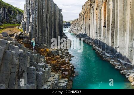 Wanderfrau mit Rucksack genießt den Studlagil Canyon. Einzigartige Jokulsa Basaltkolen und EIN Brufluss. Spektakuläre Outdoor-Szene von Island, Europa Stockfoto