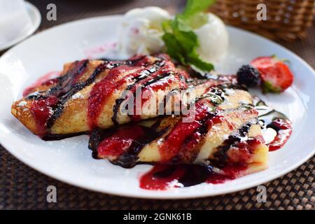 Crepes gefüllt mit Früchten und bedeckt mit Schokolade und Beerensirupen. Serviert mit Eiskugeln und Erdbeeren. Dünne Pfannkuchen, Blini. Süßer Desse Stockfoto