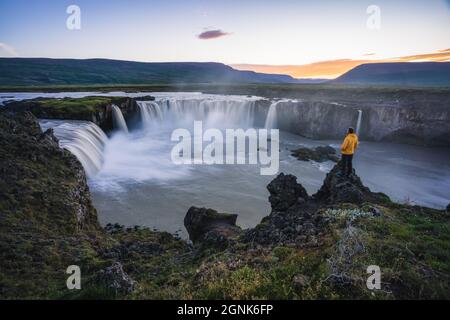 Die Luftaufnahme eines Mannes Wanderer genießen schönen Wasserfall von Godafoss bei Sonnenuntergang Licht. Island in der Sommersaison Stockfoto